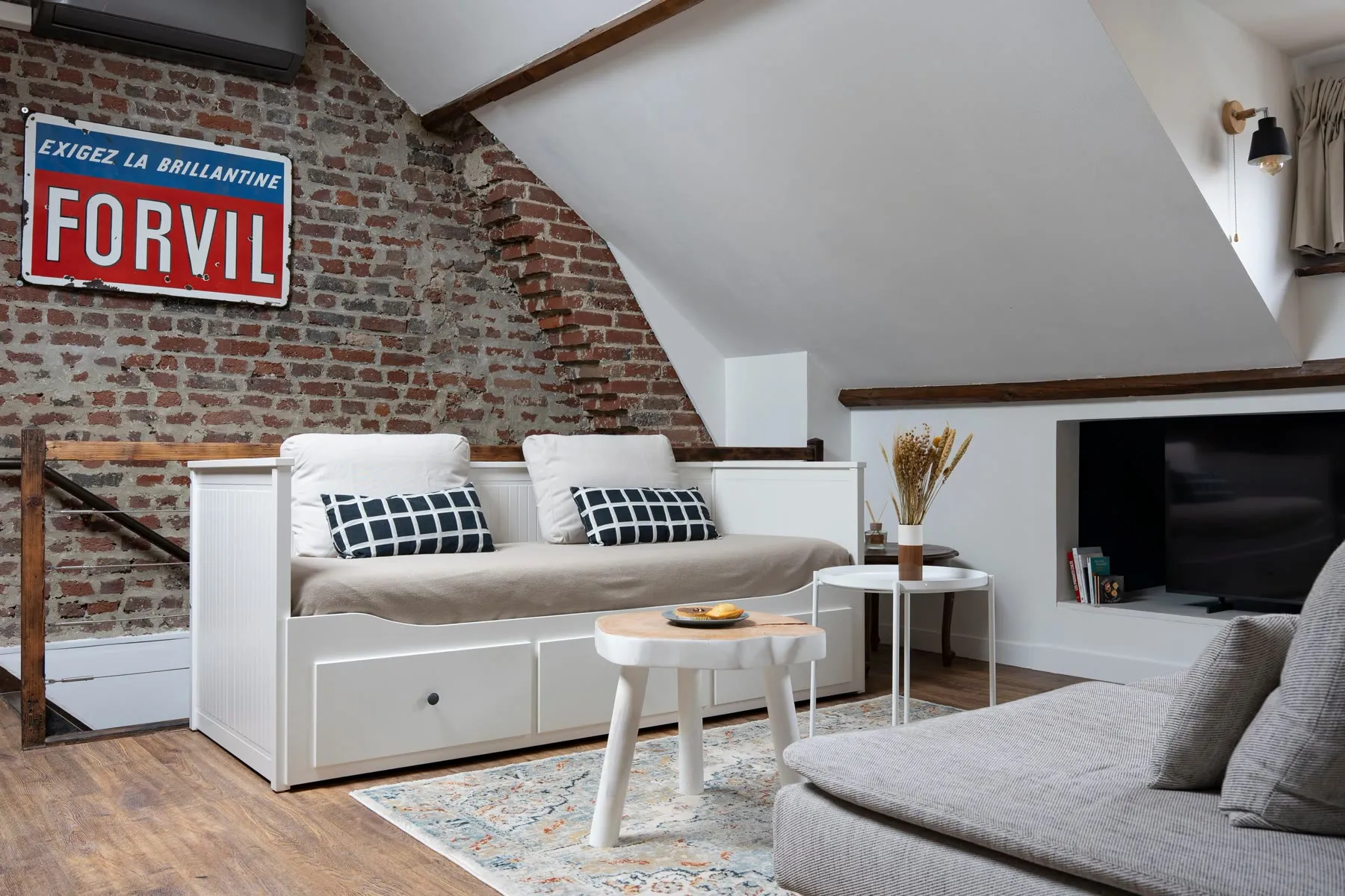 Salon du Loft d'Alfred à Lens, canapé sous les poutres et enseigne ancienne sur le mur de briques